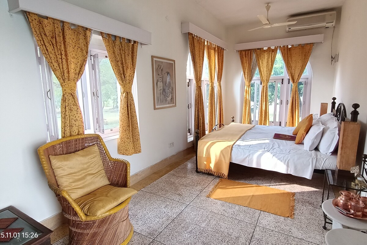 Una habitación de hotel con una cama, una silla, una mesita con ollas de cobre y cortinas.
