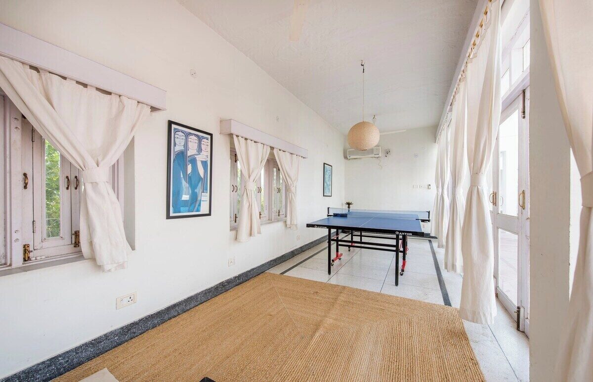 A room with a ping pong table, white curtains, and a large window.