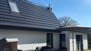 A house with a sloped roof, a covered patio area with outdoor furniture, and a small window.