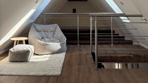 A loft bedroom with exposed wooden beams, a skylight, a staircase, and a cozy seating area with cushions.