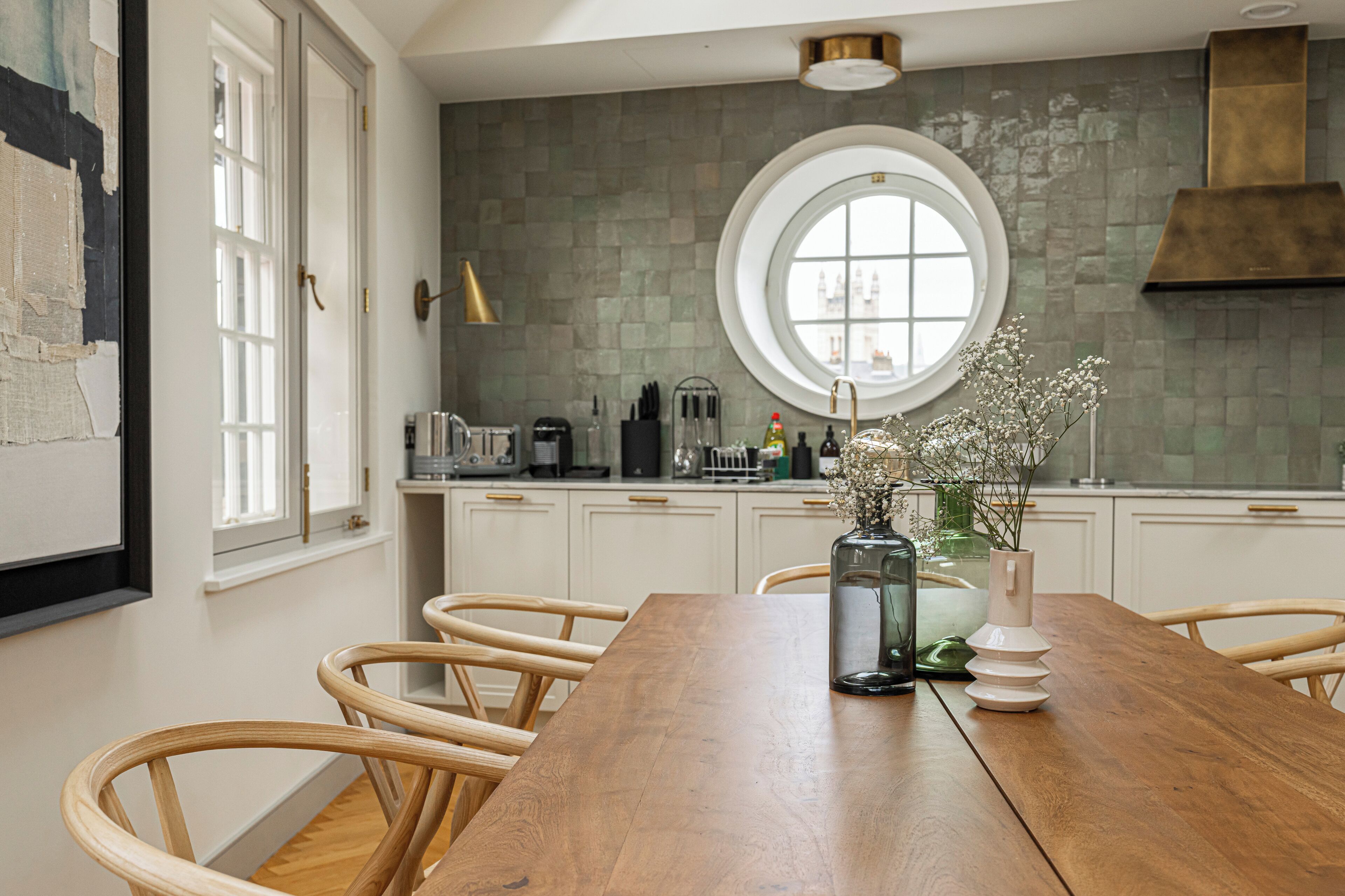 Eine Küche mit Holztisch, weißen Schränken, einem runden Fenster und einer Blumenvase.