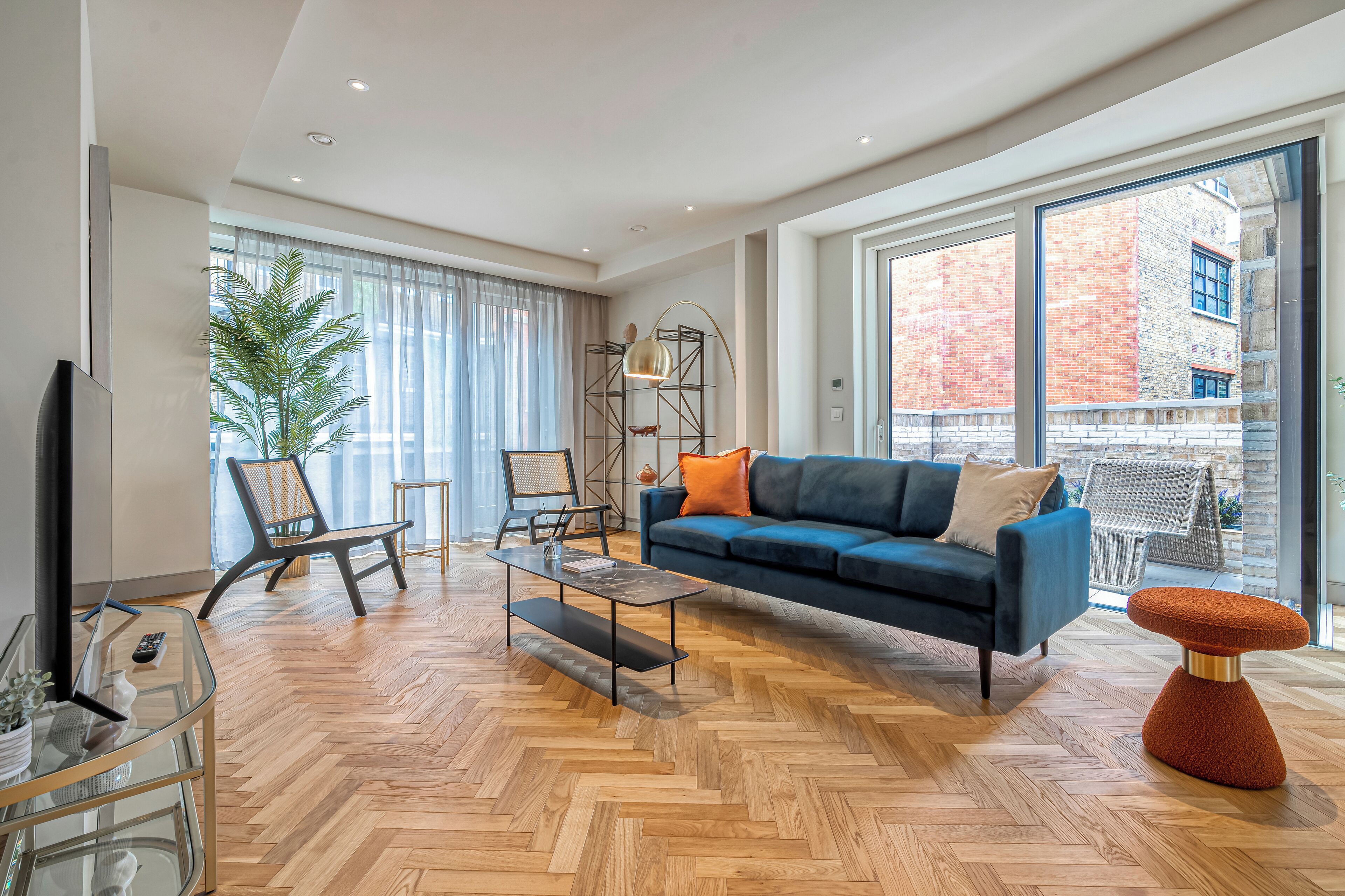 Una sala de estar moderna con un sofá azul, una mesa de centro de vidrio y un piso de madera en patrón espiga.