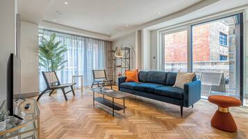 Una sala de estar moderna con un sofá azul, una mesa de centro de vidrio y un piso de madera en patrón espiga.
