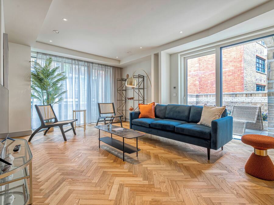Una sala de estar moderna con un sofá azul, una mesa de centro de vidrio y un piso de madera en patrón espiga.