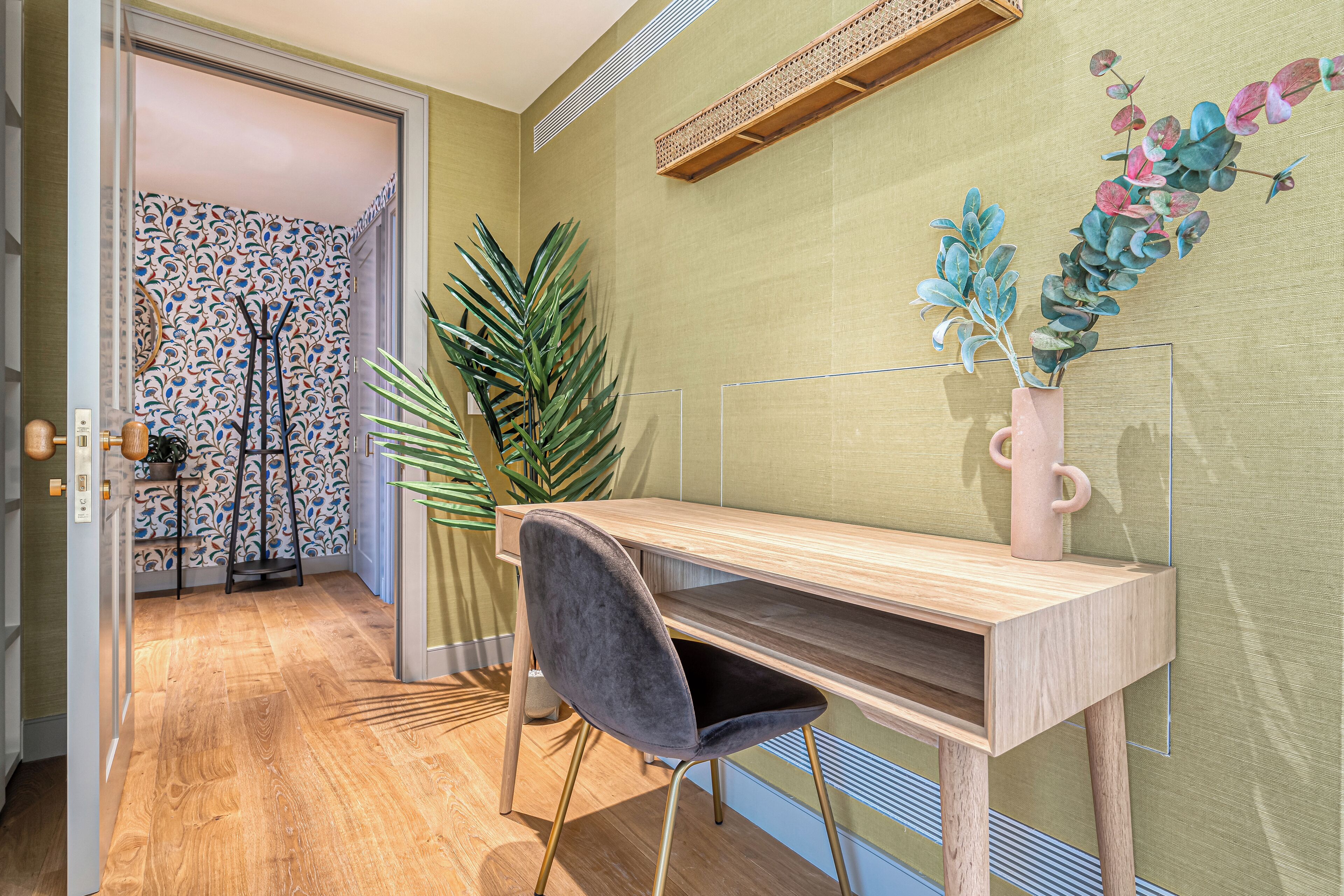 A modern office space with a wooden desk, a grey chair, and a large green plant.