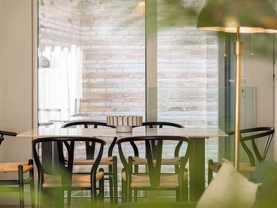 A dining area with a brick wall, a glass table, and chairs with woven seats.