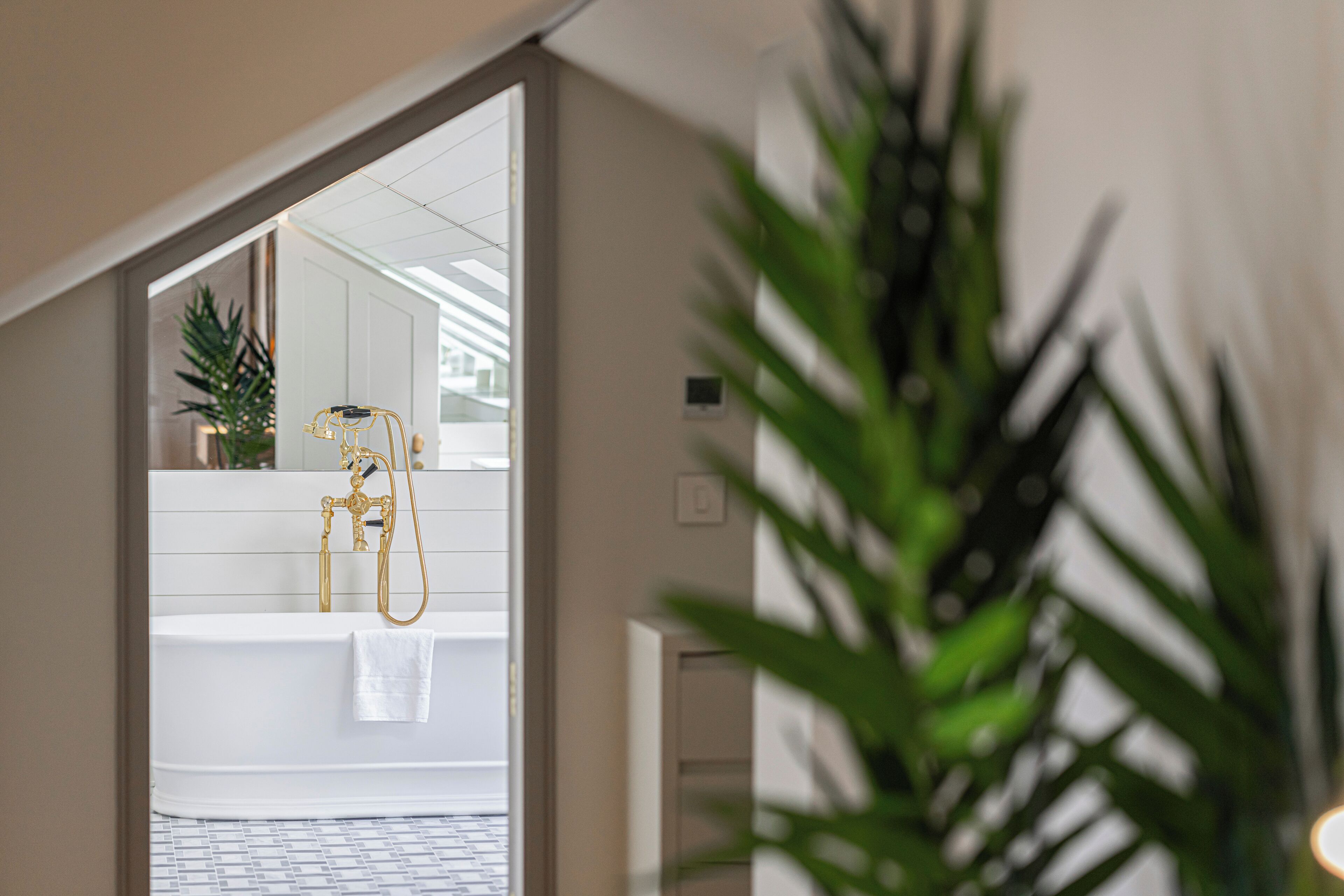 Un baño moderno con una bañera blanca, un cabezal de ducha dorado y una planta en maceta.
