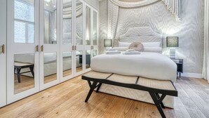 Ett sovrum med en stor säng, en bänk, en garderob med spegeldörrar och en taklampa.