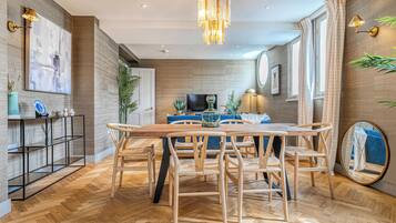 A modern dining area with a wooden table and chairs, a chandelier, and a wall-mounted lamp.