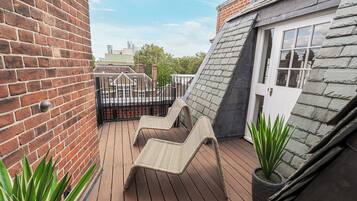 A rooftop deck with two lounge chairs, a potted plant, and a view of the city skyline.