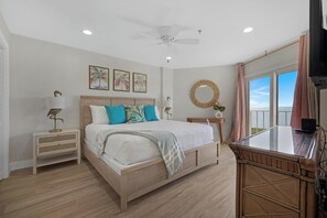 A bedroom with a bed, bedside tables, a ceiling fan, artwork, a round mirror, and a window with curtains. - Salty Mermaid Ocean Pointe 4406 (Tavernier)