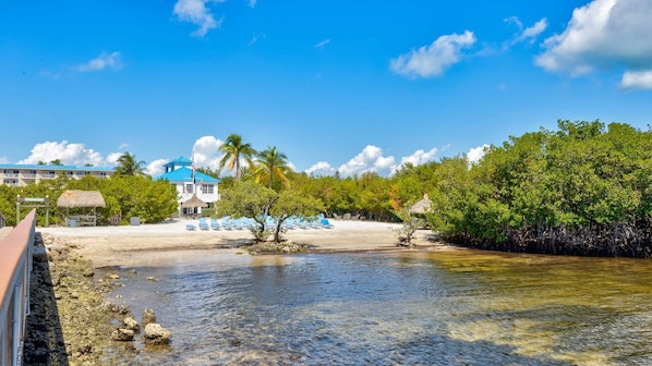 A beach resort with a clear view of the ocean, a thatched-roof hut, and a building with a blue roof.