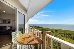 A balcony with a wooden table and chairs, a glass door leading to a room with a sofa and cushions, and a view of the sea. - Salty Mermaid Ocean Pointe 4406 (Tavernier)