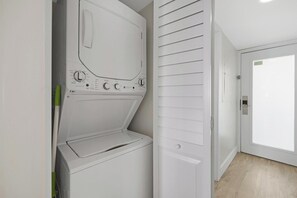 A laundry room with a washing machine and dryer, a door with a handle, and a light switch on the wall. - Salty Mermaid Ocean Pointe 4406 (Tavernier)