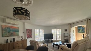 Ein geräumiges Wohnzimmer mit großem Esstisch aus Holz, beigen Sofas, einem Flachbildfernseher und Kunstwerken an den Wänden.