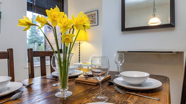 A dining table set with plates, cutlery, a vase of yellow flowers, and a wine glass. - Beeston Central House - near shops and University (Beeston)