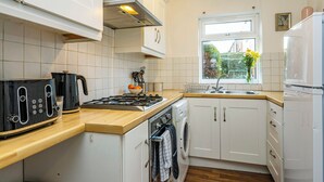 A compact kitchen with white cabinets, a wooden countertop, a built-in washing machine, and a window with a view of greenery. - Beeston Central House - near shops and University (Beeston)
