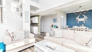 A spacious living room with a high ceiling, a staircase, and a kitchen area. - Welcome to your dream bay-view townhouse, where relaxation meets excitement. Sleep 12 guests. Linens included. Vacation at the shore with Shoreline Properties (Ocean City)