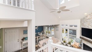 A spacious living area with a high ceiling, a ceiling fan, a fireplace, and a large TV mounted on the wall. - Welcome to your dream bay-view townhouse, where relaxation meets excitement. Sleep 12 guests. Linens included. Vacation at the shore with Shoreline Properties (Ocean City)