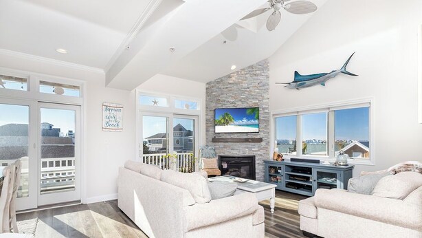 A spacious living room with a fireplace, a large TV, and a balcony with a view of the city. - Welcome to your dream bay-view townhouse, where relaxation meets excitement. Sleep 12 guests. Linens included. Vacation at the shore with Shoreline Properties (Ocean City)