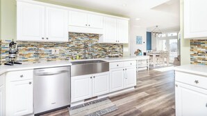 A modern kitchen with white cabinets, a stainless steel sink, and a mosaic backsplash. - Welcome to your dream bay-view townhouse, where relaxation meets excitement. Sleep 12 guests. Linens included. Vacation at the shore with Shoreline Properties (Ocean City)
