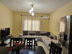 Ein Wohnzimmer mit einer Couch, einem Esstisch mit Stühlen, einem Fernseher und einem Kühlschrank.