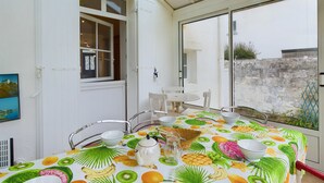 Un coin repas avec une table dressée pour quatre personnes, agrémenté d’une nappe à motifs tropicaux, de chaises blanches et d’une table blanche.