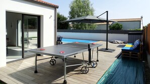 An outdoor pool area with a ping pong table, a covered seating area, and a view of a swimming pool. - House 6 with heated pool in St-Hilaire (Saint-Hilaire-de-Riez)