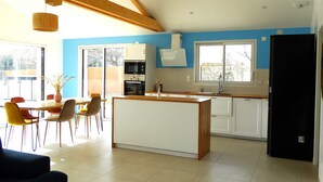 A modern kitchen with a central island, a dining area with chairs, and a large window providing natural light. - House 6 with heated pool in St-Hilaire (Saint-Hilaire-de-Riez)