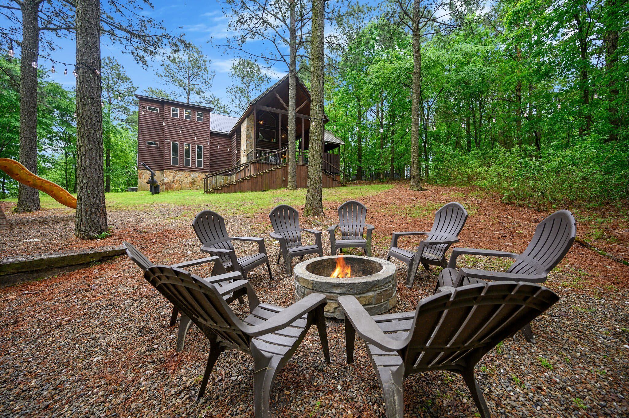 A lodge with a fire pit and Adirondack chairs in a wooded area.