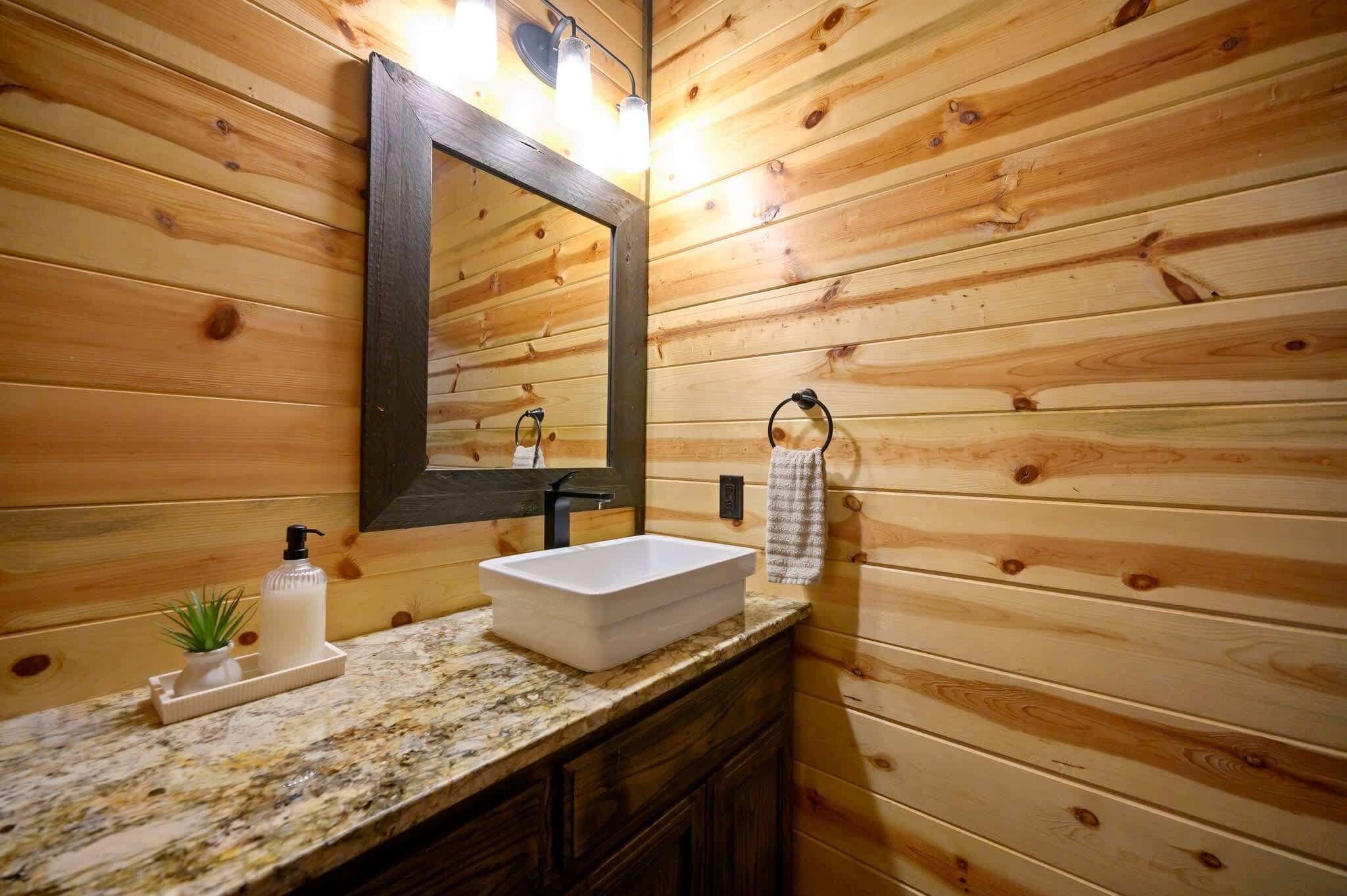 Un baño de cabaña de madera con un lavamanos blanco, un espejo y una toalla colgada en la pared.