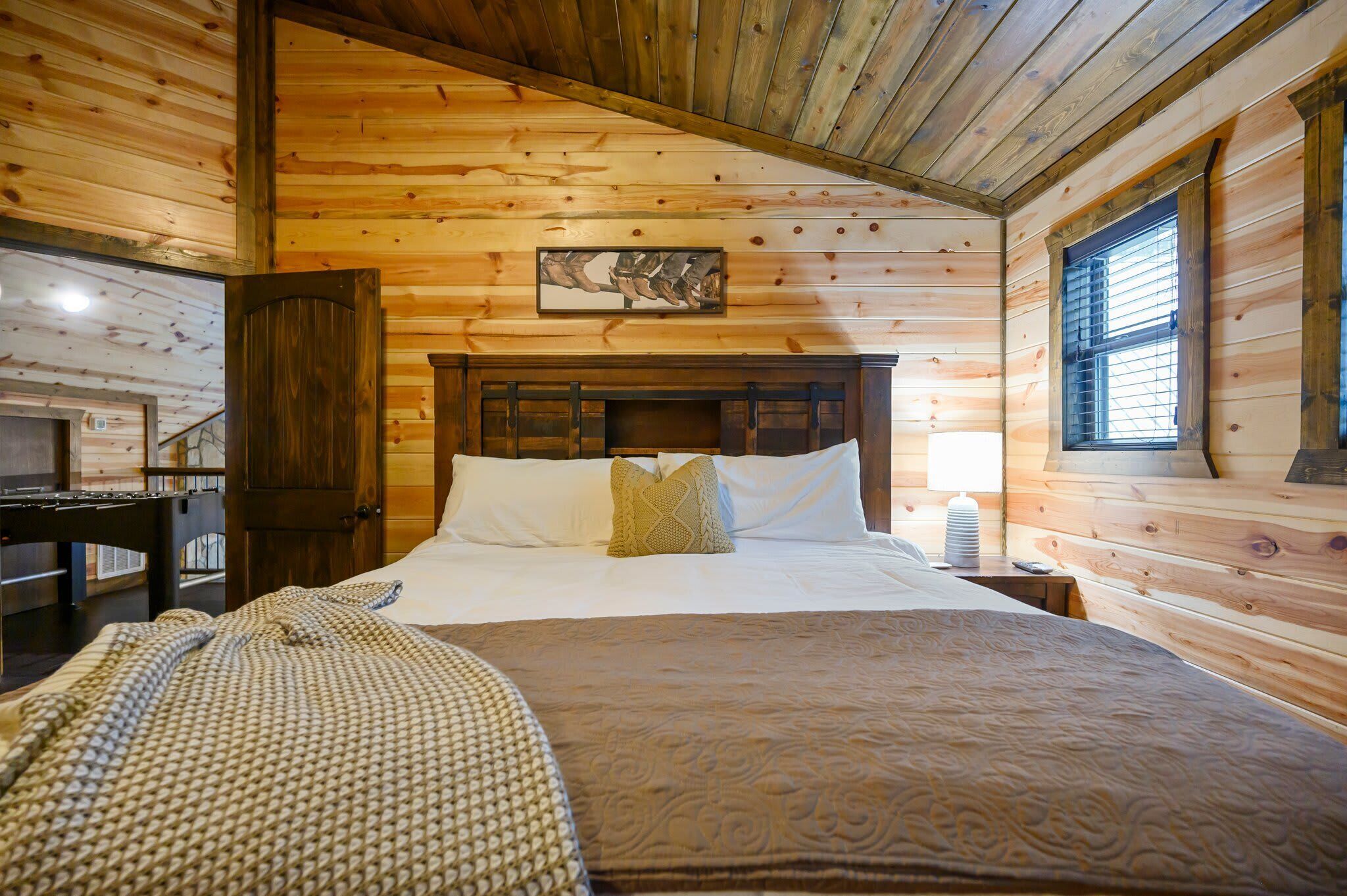 A wooden cabin bedroom with a bed, a nightstand, a lamp, and a wooden door.