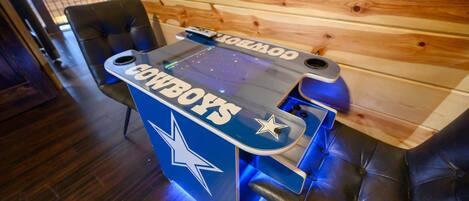 A foosball table with a Cowboys logo, placed in a room with wooden paneling and leather seating.