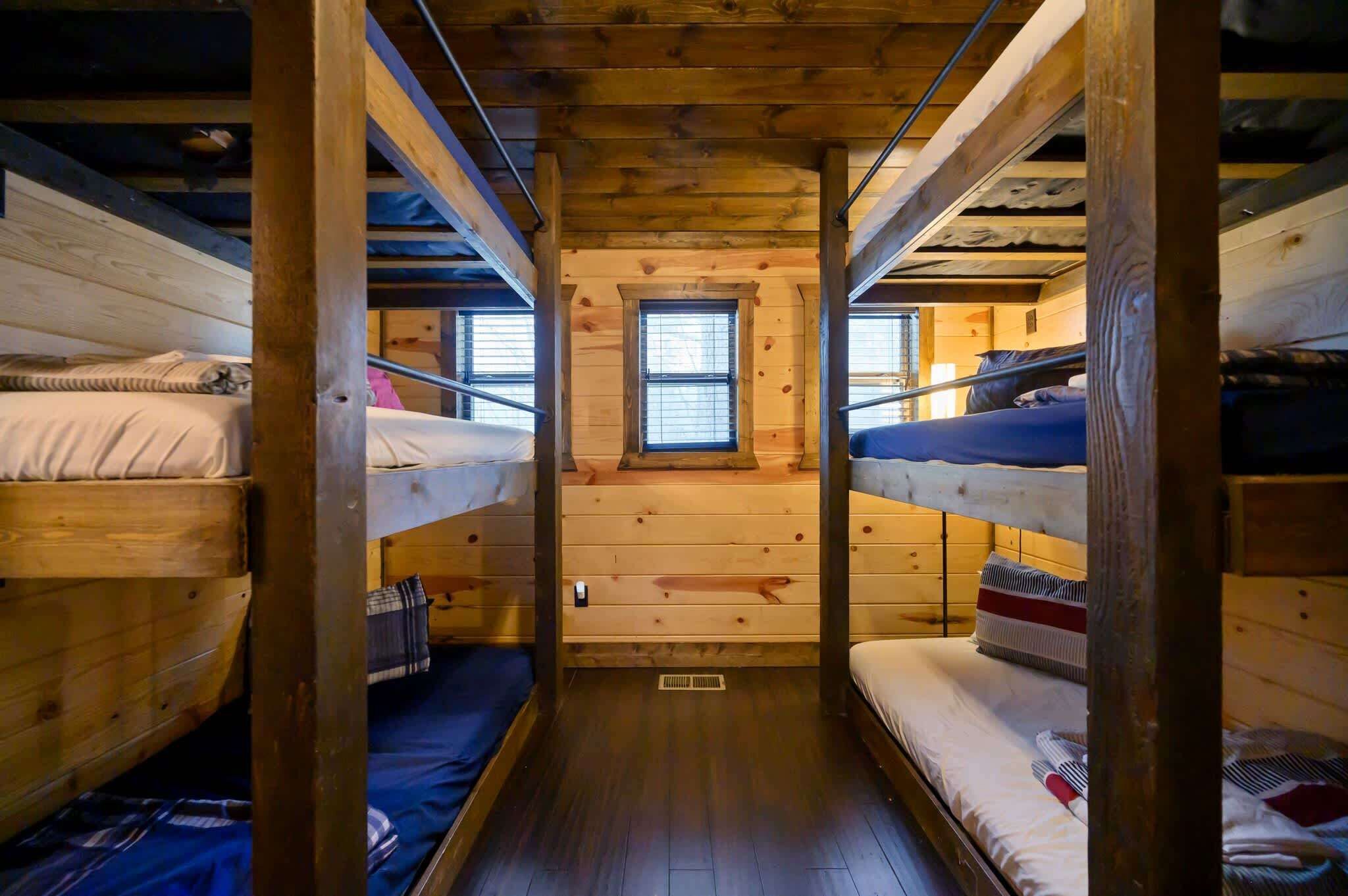A cabin with bunk beds, wooden walls, a small window, and a wooden floor.