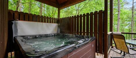 A hot tub in a covered outdoor area with a wooden deck and a table with chairs.