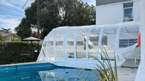 A swimming pool with a clear cover, surrounded by a white building and greenery. - Hotel Montecarlo PSH (Villa Carlos Paz)