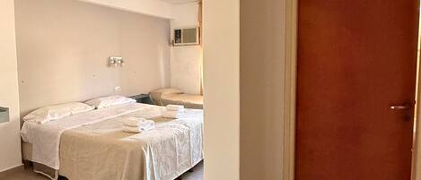 Una habitación de hotel con dos camas, una puerta de madera y suelo de baldosas.