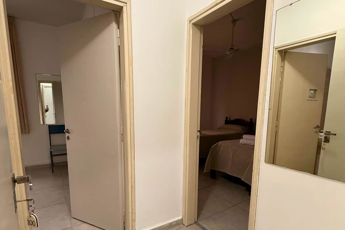 Ein Flur mit zwei geöffneten Türen, die zu einem Schlafzimmer und einem Badezimmer führen. Der Flur hat einen Fliesenboden und weiße Wände.