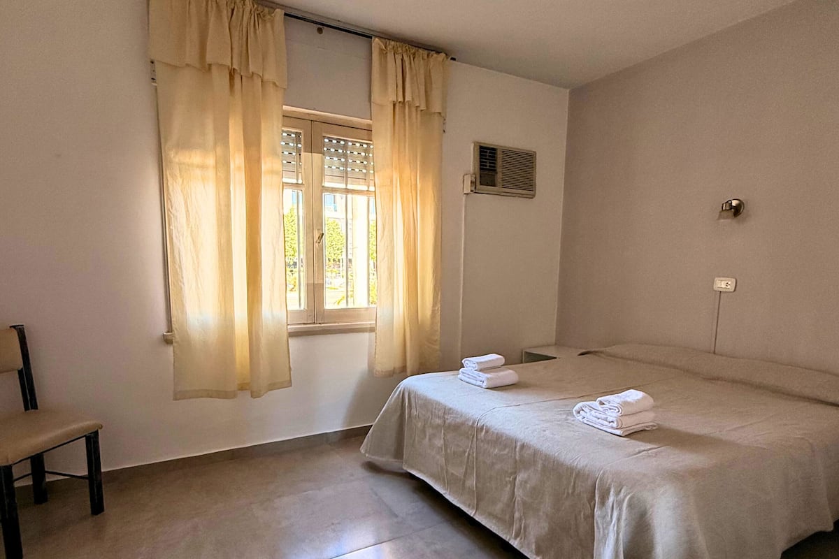 Ein Hotelzimmer mit einem Bett, einem Sessel, einem Fenster mit Vorhängen und einer Wand-Klimaanlage.