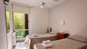 A hotel room with two beds, a ceiling fan, a small wooden nightstand, and a window with a view of greenery. - Hotel Montecarlo PSH (Villa Carlos Paz)