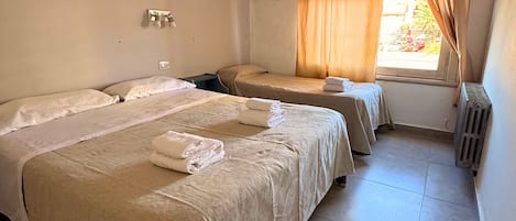 Habitación de hotel con dos camas, ropa de cama color beige, una ventana con cortinas, un equipo de aire acondicionado y un radiador.