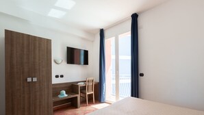 A hotel room with a bed, a desk, a chair, a TV, and a wardrobe.