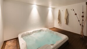 A spa room with a hot tub, wooden flooring, white walls, and a decorative vase with branches.