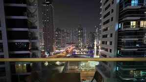 Un balcón con mesa y sillas que da a una vista nocturna de la ciudad.