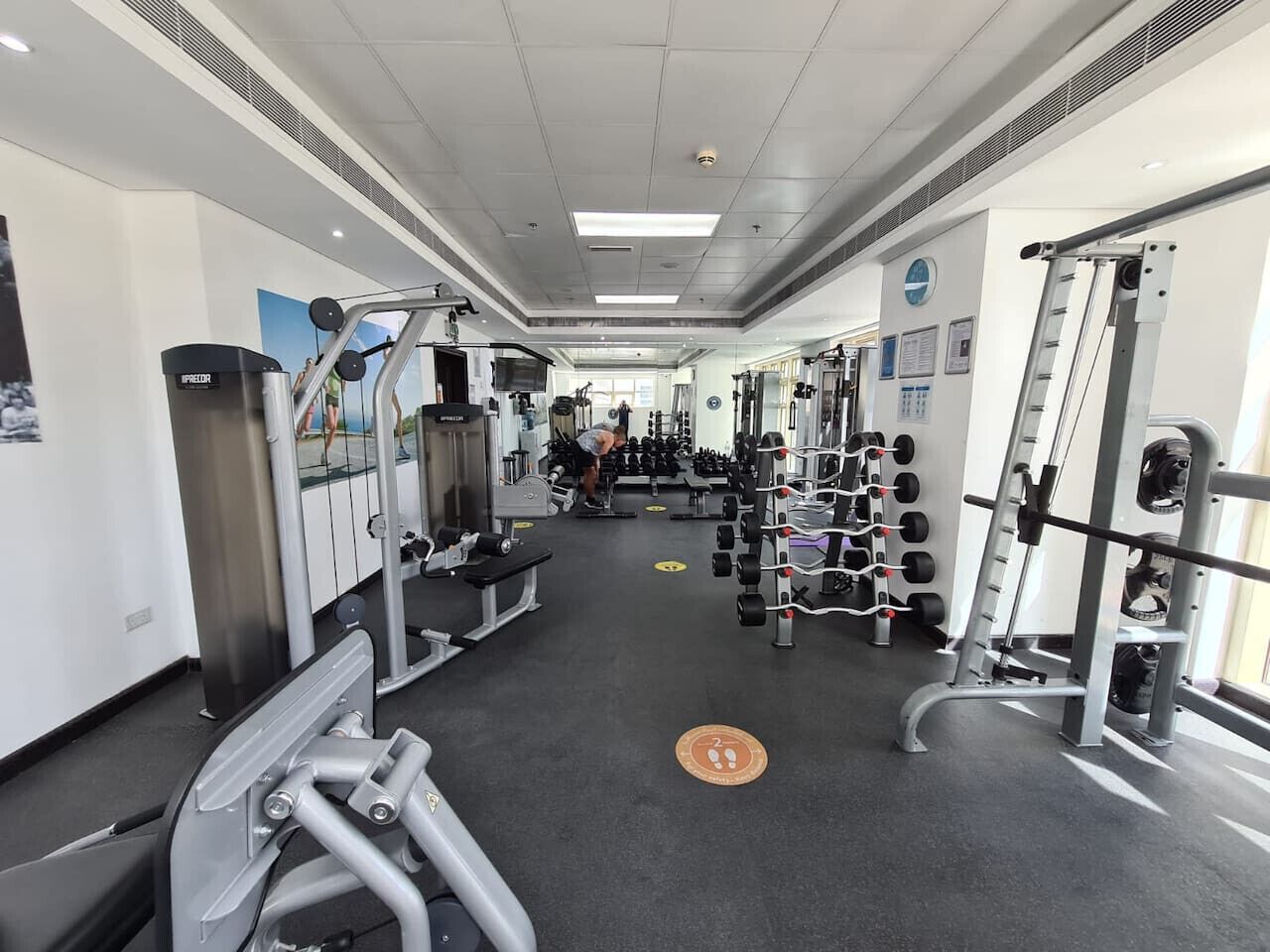 Une salle de sport équipée de divers appareils d’entraînement, notamment des machines à poids et des poids libres, disposés dans un espace vaste et bien aménagé.