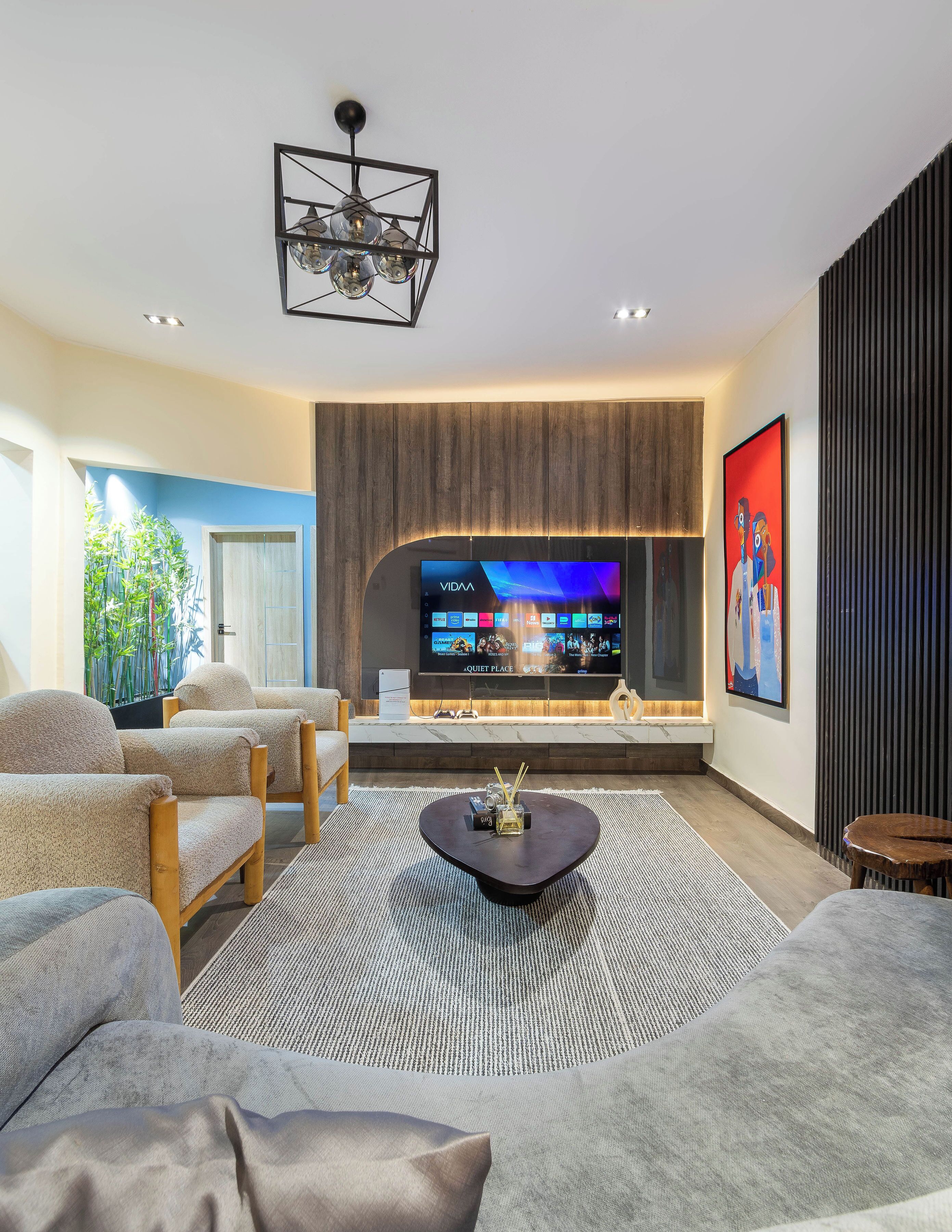 A modern living room with a flat-screen TV, comfortable seating, and a decorative light fixture.