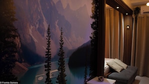 Quarto com um grande mural de paisagem montanhosa, um sofá cinza e uma pequena mesa com um objeto decorativo.