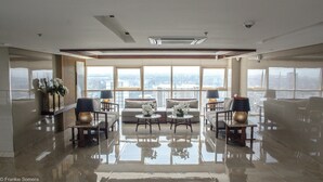 Ampla sala de estar com teto alto, grandes janelas com vista para a cidade e piso refletivo.