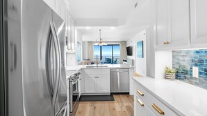 A modern kitchen with white cabinetry, a stainless steel refrigerator, and a view to the outside. - 302C - 2 bedroom and 2 bath newly remodeled (ORANGE BEACH)