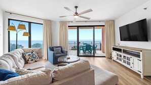 A modern living room with a sofa, armchair, and coffee table, a flat-screen TV, and a balcony with a view of the sea. - 302C - 2 bedroom and 2 bath newly remodeled (ORANGE BEACH)